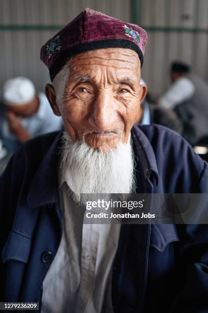a man wearing a uyghur white hat and a white beard in kuche, xinjiang leaned on the table and smiled at the camera - emo guy stock pictures, royalty-free photos & images