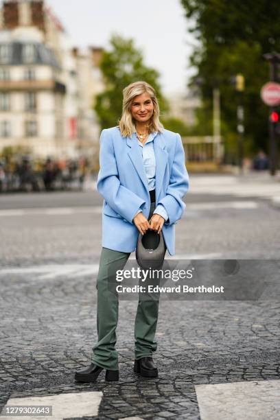 Xenia Adonts wears a blue oversized blazer jacket, a blue shirt, a black bag, green flare pants, black shoes, outside Coperni, during Paris Fashion...