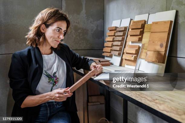 smiling woman holding wood tile while sitting by desk at office - designer einrichtung stock-fotos und bilder