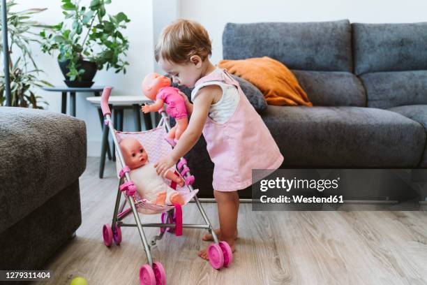 cute baby girl putting toys in baby stroller while standing at home - prams stock pictures, royalty-free photos & images