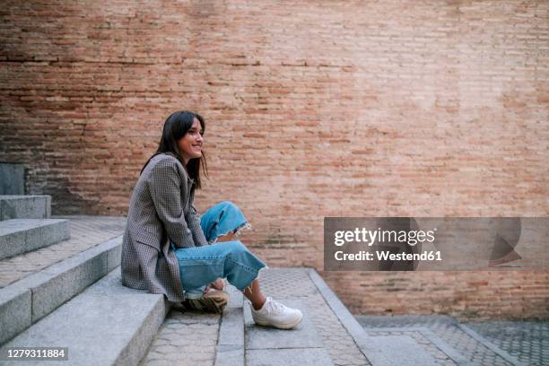 smiling young woman sitting on staircase - blazer stockfoto's en -beelden