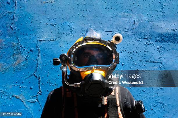 close-up of male instructor wearing diving suit standing against blue wall - tiefseetauchen stock-fotos und bilder