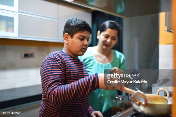preadolescent boy helping her mother in the kitchen - indian mom stock-fotos und bilder