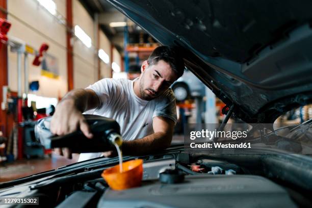 auto mechanic filling engine oil while standing in garage - auto mechaniker stock-fotos und bilder