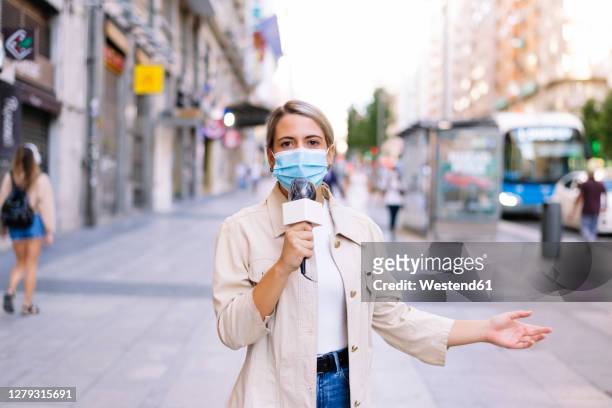 female reporter wearing mask talking over microphone on street in city - reportero fotografías e imágenes de stock