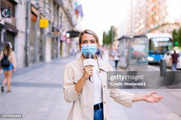 female reporter wearing mask talking over microphone on street in city - tv reporter 個照片及圖片檔