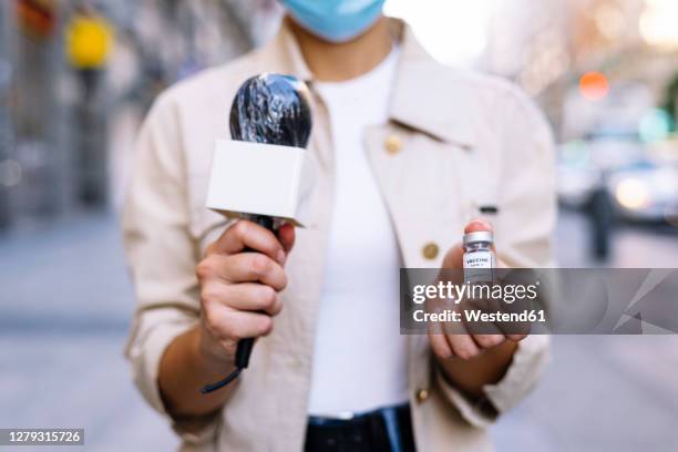 close-up of female reporter wearing mask showing vaccine vial while standing outdoors - science journalism stock pictures, royalty-free photos & images