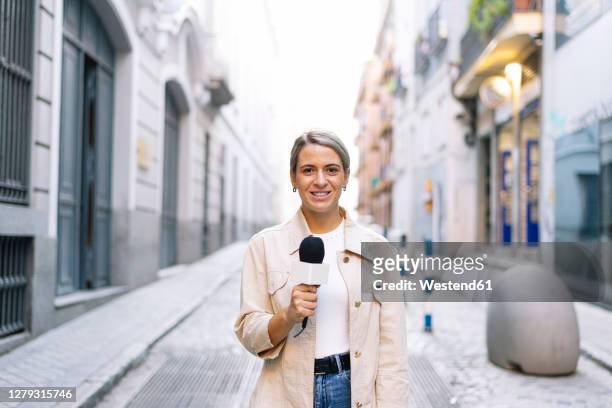 female journalist talking over microphone while standing on street in city - journalist stock-fotos und bilder