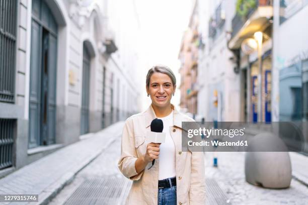 female journalist talking over microphone while standing on street in city - journalist photos et images de collection