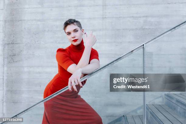 confident trans man wearing red dress standing on steps against wall - men wearing dresses stock-fotos und bilder