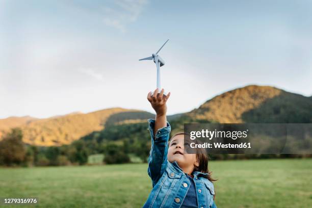 cute girl playing with wind turbine toy while standing at backyard - energia eolica fotografías e imágenes de stock