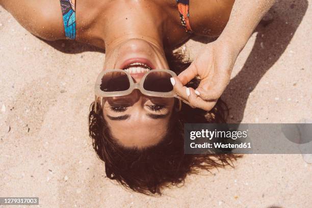 cheerful woman wearing sunglasses while lying at valdevaqueros beach on sunny day, tarifa, spain - sunglasses top view stock pictures, royalty-free photos & images