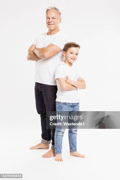 father and son with arms crossed posing while standing against white background - boy jeans stockfoto's en -beelden