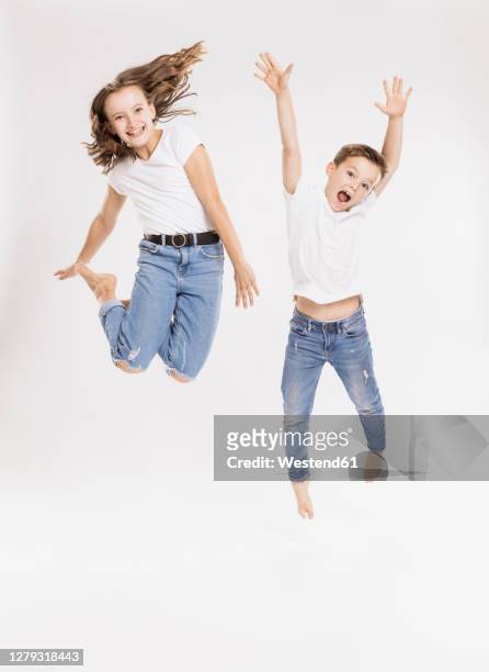 cheerful siblings jumping against white background - boy jeans stockfoto's en -beelden