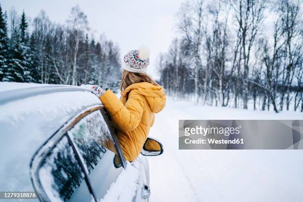 woman looking at bare trees while leaning out through car window during winter - winter car window stock-fotos und bilder