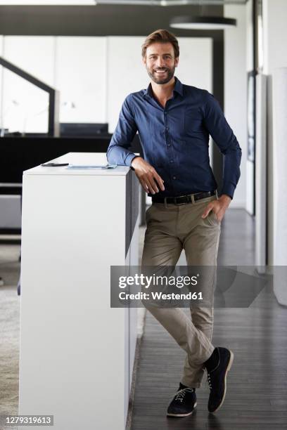 businessman smiling while standing at office - leaning stock pictures, royalty-free photos & images