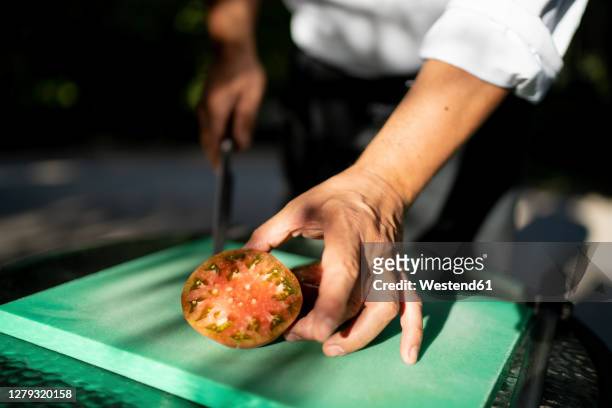 close-up of male chef holding tomato slice on cutting board in orchard - pomar imagens e fotografias de stock