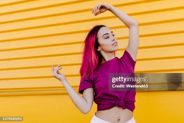 young woman with dyed hair looking away while dancing against yellow wall - purple shirt - fotografias e filmes do acervo