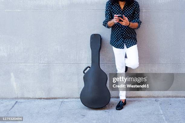 guitarist using mobile phone while standing against concrete wall - guitar case fotografías e imágenes de stock