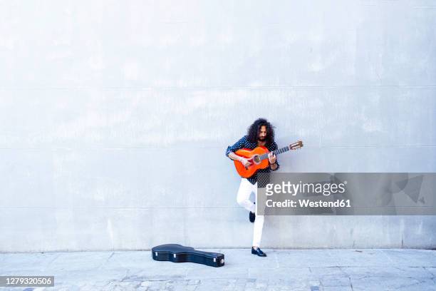 man playing guitar while standing against concrete wall - étui à guitare photos et images de collection