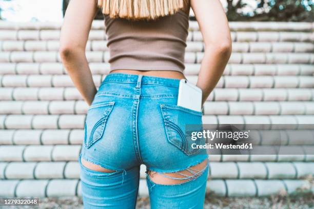 close-up of young woman with smart phone in jeans pocket - jeans back stockfoto's en -beelden