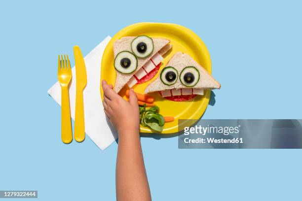 hand of baby girl picking up funny looking sandwich withanthropomorphic face - baby food fotografías e imágenes de stock