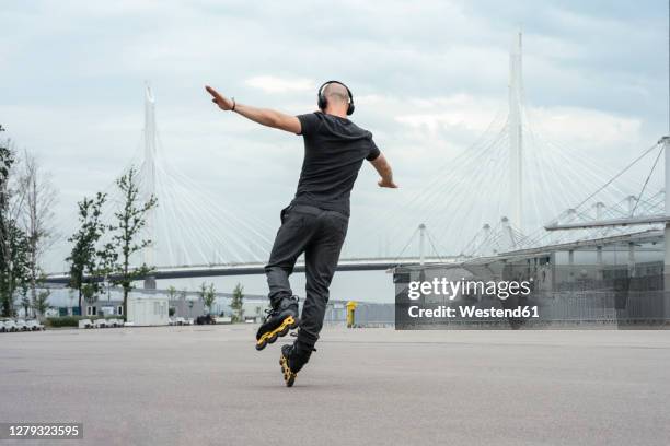 young man with arms outstretched listening music while inline skating on road - inline skate 個照片及圖片檔