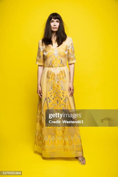 mature woman wearing dress standing against yellow background - robe jaune photos et images de collection