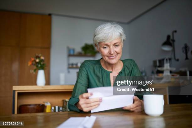 senior woman reading letter while sitting at home - old woman sitting stock-fotos und bilder