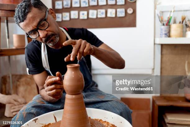 close-up of male potter making earthenware while sitting in workshop - pottery wheel photos et images de collection
