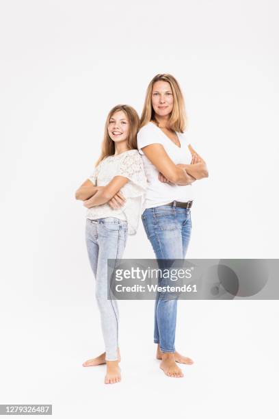 mother and daughter with arms crossed standing back to back against white background - kids standing stock-fotos und bilder