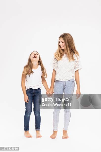 cheerful sisters holding hands while standing against white background - 12 13 jahre mädchen stock-fotos und bilder