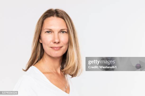 close-up of smiling mature woman with blond hair against white background - 40s woman t shirt studio stock pictures, royalty-free photos & images