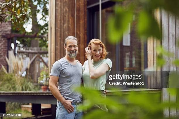 smiling couple standing in front of tiny house at yard - three quarter length stockfoto's en -beelden