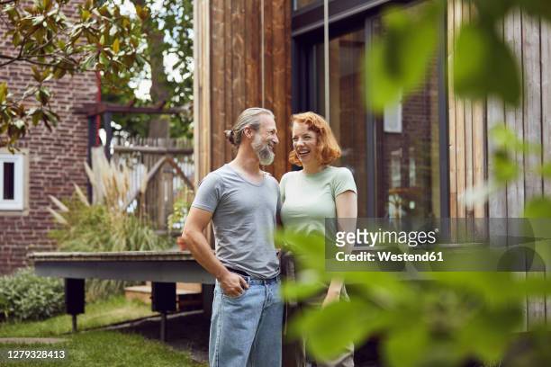 cheerful couple looking at each other while standing in front of tiny house - mann vor haus stock-fotos und bilder
