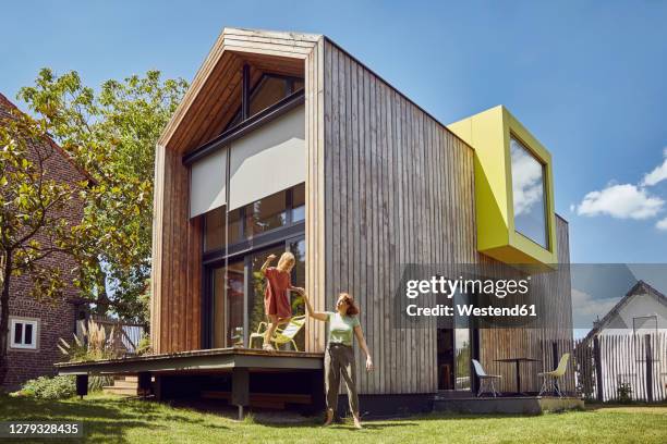 mother assisting daughter in jumping outside tiny house at yard - sustainable lifestyle family stock pictures, royalty-free photos & images