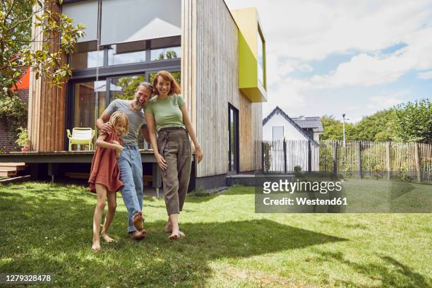 cheerful parents with daughter standing against tiny house in yard - two parents stock-fotos und bilder