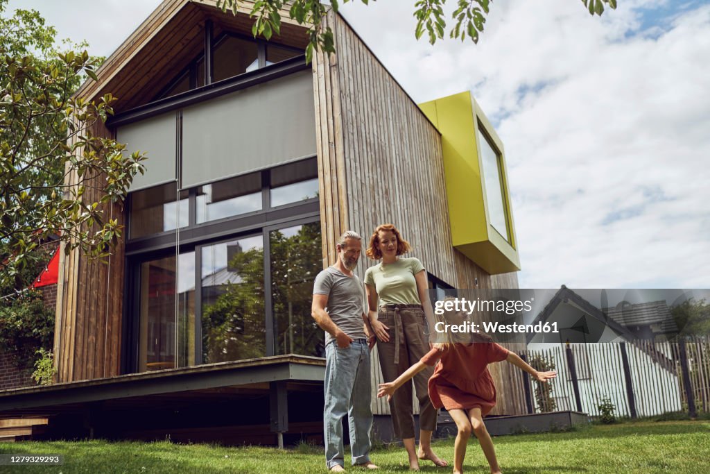 Parents looking at daughter with arms outstretched dancing in yard