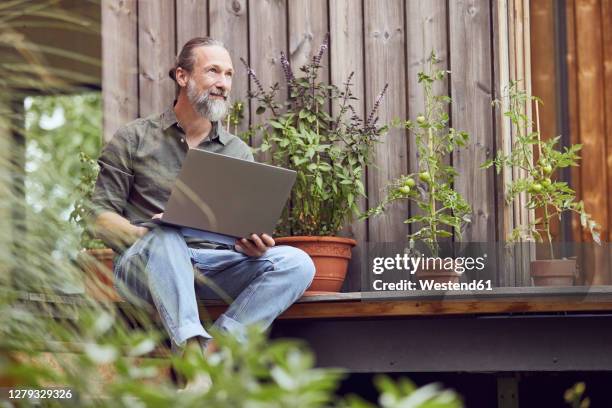 thoughtful bearded man with laptop sitting outside tiny house - mann vor haus stock-fotos und bilder