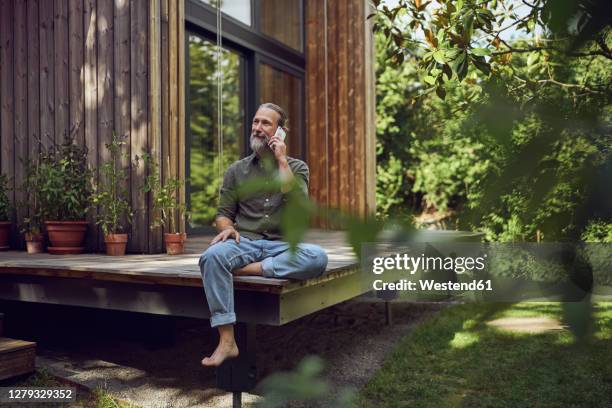 mature man looking away while talking over mobile phone outside tiny house - eco house stockfoto's en -beelden