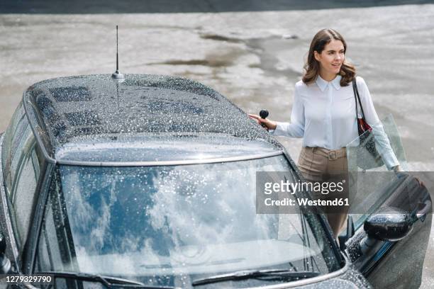 young woman opening door of car while standing at parking lot - entrando fotografías e imágenes de stock