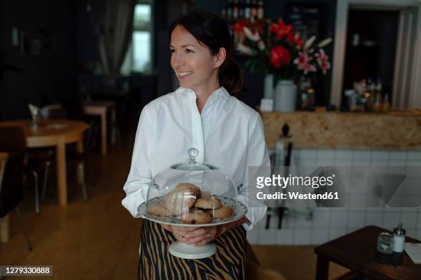 smiling female owner holding cookies in plate with cloche at cafe - cloche stock pictures, royalty-free photos & images
