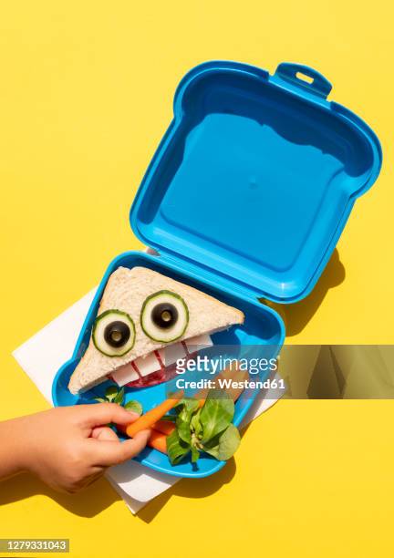 hand of baby girl picking up baby carrot from lunch box with funny looking sandwich with anthropomorphic face - ベビーキャロット ストックフォトと画像