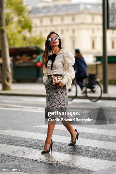 Phuong Thythu wears sunglasses, a white ruffled shirt with puff sleeves, a bow tie / lavaliere, a belt, a Petite Malle Vuitton bag, a black and white...