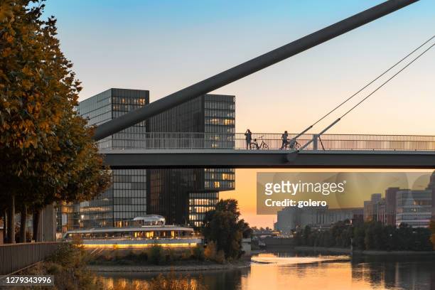 silhouettes on bridge over rhine river in düsseldorf in early fall season - medienhafen stock pictures, royalty-free photos & images