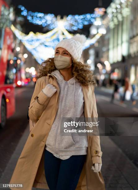 woman enjoying the christmas lights in the city while walking on the street wearing a facemask - retail covid stock pictures, royalty-free photos & images