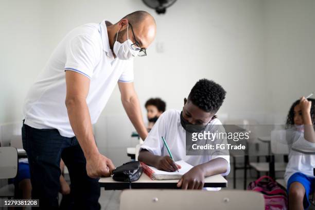 Teacher helping student at classroom using face mask
