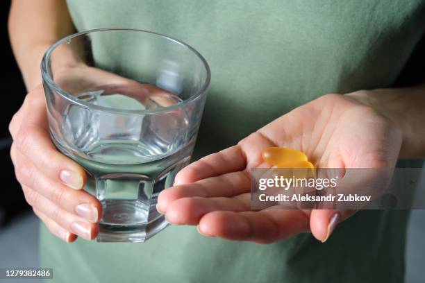 the woman is holding omega-3 fish oil capsules or medications, and a glass of water. healthy lifestyle, prevention and treatment of diseases. the girl takes and drinks food supplements and vitamins. biologically active additive. - fish oil stock photos et images de collection