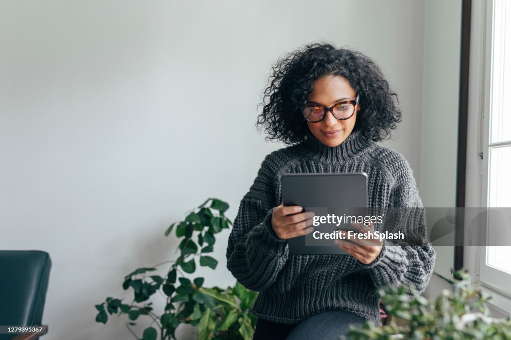 Arbeiten von zu Hause aus: Eine junge Frau, die ein digitales Tablet einspielt, um etwas zu lesen/beobachten