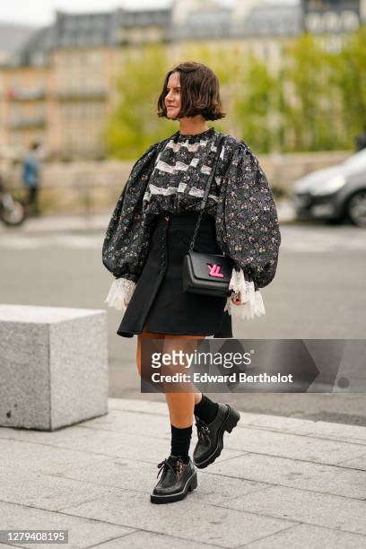 Marta Cygan wears a gray floral print ruffled top with puff sleeves and lace, a black skirt, a black leather Vuitton bag with neon pink logo, black...